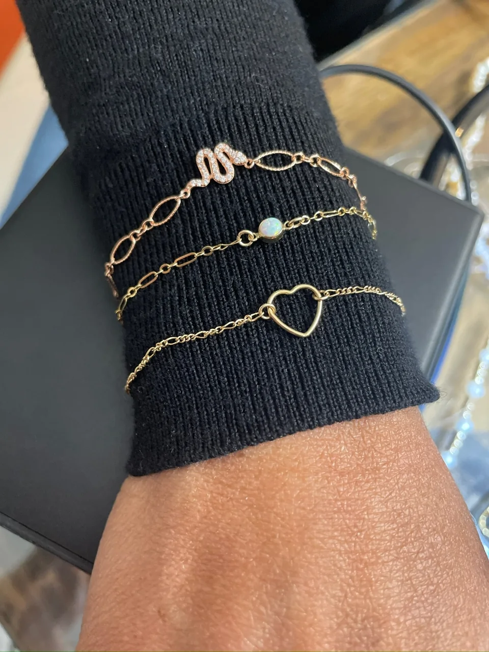 Stack of three gold permanent bracelets with snake, opal and heart motifs over a black sleeve