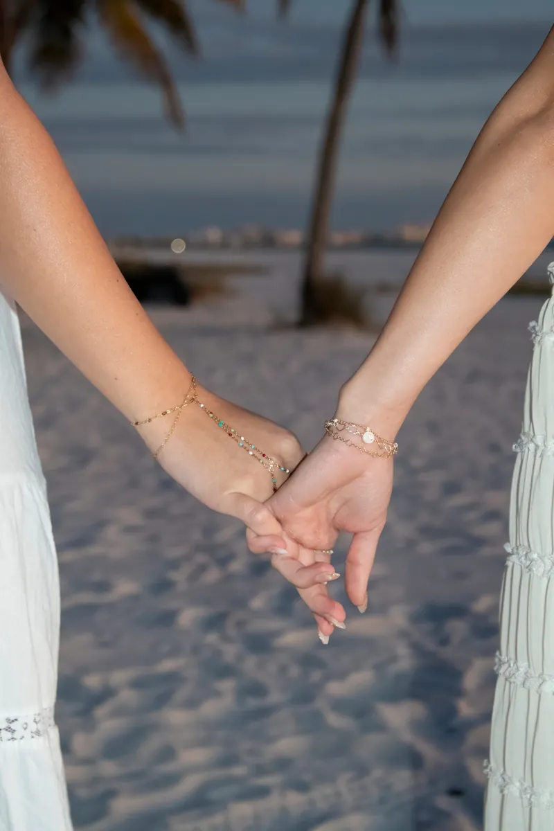 Two people holding hands at dusk wearing gold permanent bracelets and a hand-chain