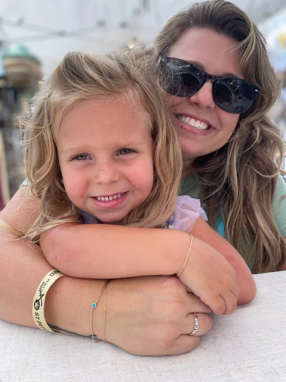 A mother and daughter hugging, both wearing matching gold permanent bracelets