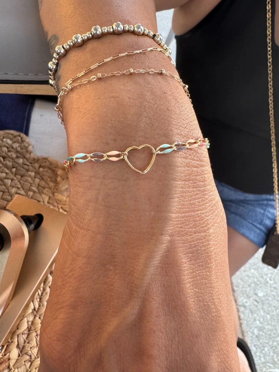 Delicate stacked gold and pastel permanent bracelets on a sun-kissed wrist